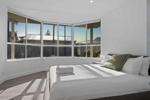 a white bed in a room with large windows at The Beachside Gathering in Anna Bay