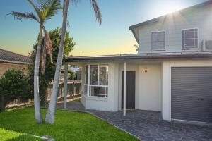a white house with a garage and palm trees at The Beachside Gathering in Anna Bay