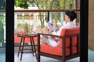a man sitting in a chair reading a book at March Hotel & Suite Riverside in Chiang Mai