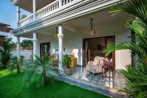 a house with a porch with a chair and palm trees at SaffronStays Sweet Mango - 4BR Goan Villa w Private Pool, Mango Garden, Bar Gazebo & Vibrant Interiors Near Beaches in Parra +52 photos