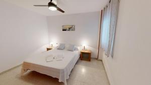 a white bedroom with a bed and a ceiling fan at Apto Mar Blau in L'Ampolla +2 photos