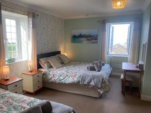 a bedroom with two beds and a desk and two windows at Haelarcher Farmhouse and Helicopter B&B in Lizard