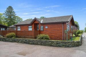 a wooden cabin with a stone wall at Lakeside 1, White Cross Bay, mid way between Ambleside and Windermere with hot tub in Windermere