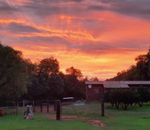 a sunset over a field with a house and a fence at Goedgelegen Retreat Cottage in Groot-Marico