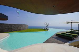 a large swimming pool with chairs and an umbrella at Nya Uluwatu in Uluwatu