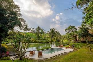 a swimming pool in a garden with chairs and a pond at Alam Taman Villa in Tabanan