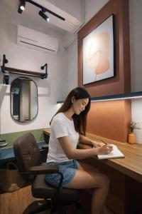 a woman sitting in a chair writing on a paper at Faloe Hostel in Kota Kinabalu