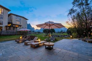 a patio with an umbrella and couches and tables at Meadowscape Resort at Yulong River - Karst Views & Infinity Pool & Tickets Reservation Service & Free Laundry in Yangshuo