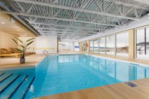 a swimming pool with blue water in a building with windows at Hôtel Baker in Gaspé