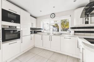 a kitchen with white cabinets and a clock on the wall at Spacious 4BDR House with Parking by Heathrow in Hillingdon