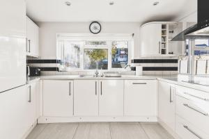 a kitchen with white cabinets and a clock on a window at Spacious 4BDR House with Parking by Heathrow in Hillingdon
