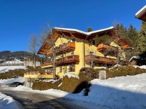 a large yellow building with snow on the ground at Julius Appartements & Zimmer in Wagrain