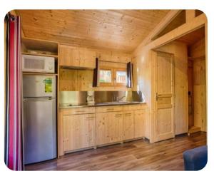 a kitchen with wooden cabinets and a stainless steel refrigerator at Cabane bois insolite vue montagne piscines famille in Laruns
