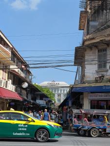a yellow and green car driving down a city street at Happy Hope Khao San in Bangkok