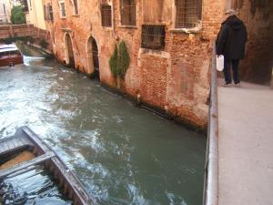 a person standing on a ledge next to a canal at Ca' Emma in Venice