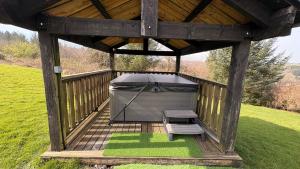 a gazebo with a grill and a bench on a field at Bryn Bettws Log Cabins Ltd in Port Talbot