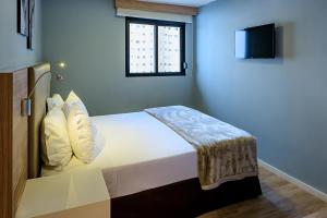 a bedroom with a white bed with a window at Rio Hotel by Bourbon Batel - Curitiba in Curitiba