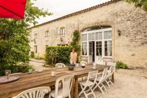 a woman standing outside of a building with a wooden table and chairs at Le Pistoulet Gîte in Doeuil-sur-le-Mignon
