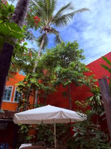 a white umbrella in front of a red building with a palm tree at Imperialis Boutique Hotel in Canavieiras