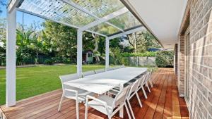 a white pergola on a deck with a table and chairs at Gemburra By Holidayco in Pearl Beach
