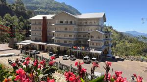 a large white building with cars parked in a parking lot at Kingswood Tea Factory in Ramboda