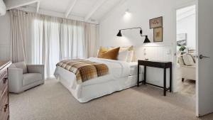 a white bedroom with a large bed and a chair at Malmsbury Cottage in Malmsbury