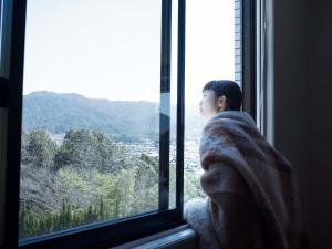 a woman in a blanket looking out of a window at Hotel Espacio 山口 -ADULT ONLY- in Yamaguchi
