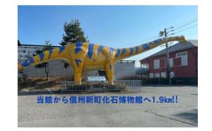 a large yellow dinosaur statue in a parking lot at 古民家白馬 in Nagano