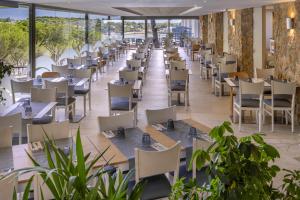 an empty restaurant with tables and chairs and plants at GHT S'Agaró Mar Hotel in Sant Feliu de Guíxols