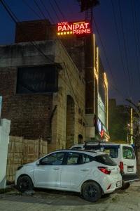 two cars parked in front of a building with a neon sign at Hotel Panipat Prime in Pānīpat