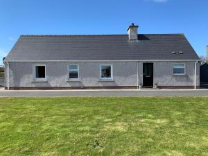 a gray house with a green lawn in front of it at Heatherlea Cottage in Skigersta