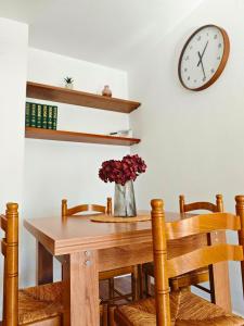 a dining room table with a vase of flowers and a clock at Apartamento Pena Furada in Ribadeo