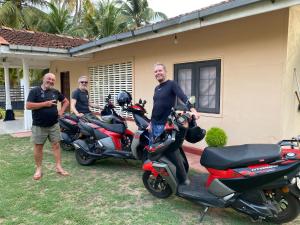 three men standing next to motorcycles parked outside a house at Gloria Cottage Non AC in Negombo