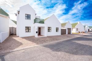 a white house with green roofs on a street at Benguela Cottage in Langebaan