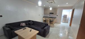 a living room with a black couch and a kitchen at Appartement 2 chambres in Selouane