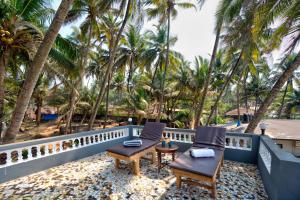 a balcony with two chairs and palm trees at Anjuna Beach House in Anjuna