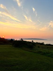 a sunset over the water with a grass field at Motel Seal Rock in Perce +5 photos