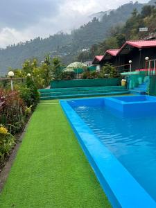 a blue swimming pool with green grass next to a house at Shivpuri Hills Camp in Jāmb