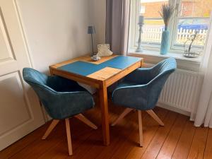 a wooden table with two blue chairs next to a window at Lütte Stuv Das Alte Pastorat in Uelvesbüll
