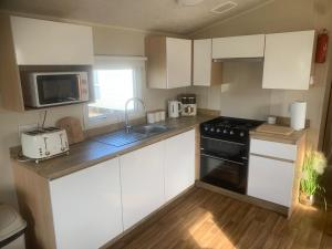 a kitchen with white cabinets and a black stove top oven at Sundaes caravan rental in Kinmel Bay