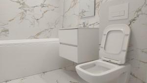 a white bathroom with a toilet and a bath tub at 85th Pool View Studio in Popeşti-Leordeni +6 photos