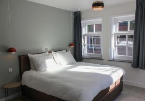 a bedroom with a bed with white sheets and two windows at Boutique Hotel Nieuw Uilenburg in Den Bosch