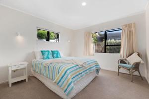a white bedroom with a bed and a chair at Spectacular Woolleys Bay in Matapouri +1 photo