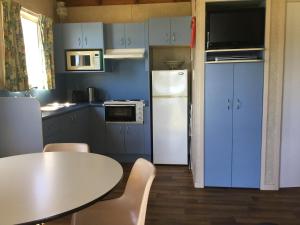 eine Küche mit blauen Schränken, einem Tisch und einem weißen Kühlschrank in der Unterkunft Riviera Caravan Park in Sussex inlet