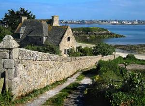 an old stone wall with a house and the water at Ty arvor in Saint-Pol-de-Léon