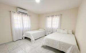 a white bedroom with two beds and two windows at Balbuena Countryside Villa with Private Pool in San Felipe de Puerto Plata +8 photos