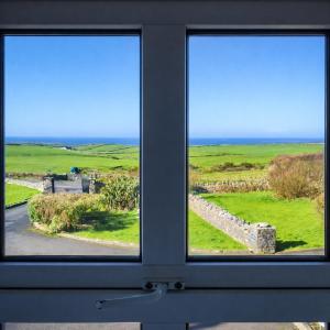 a window with a view of a field and the ocean at Aran View Holiday Homes Doolin - The Atlantic Stone House - Ocean Views in Doolin