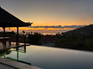 a swimming pool with a sunset in the background at First Light Villa at Lipah Beach, Amed in Amed