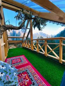 a balcony with green grass and colorful carpets at Lambri View Treehouse Jibhi in Jibhi