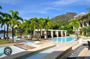 a swimming pool with palm trees and a building at Carola Pico De Loro in Nasugbu